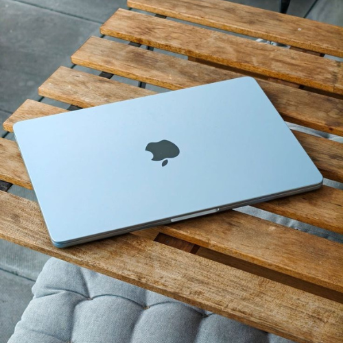 Closed silver Apple MacBook laptop on a wooden slatted table with gray cushioned chair nearby