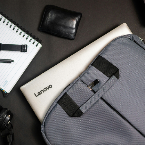 Lenovo laptop partially inside gray fabric backpack with black wallet, notebook, pen, and headphones on black surface
