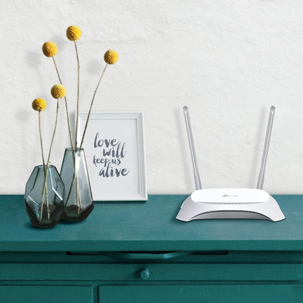 White dual-antenna wireless router on teal cabinet beside yellow billy balls in gray vases and framed love quote