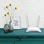 White dual-antenna wireless router on teal cabinet beside yellow billy balls in gray vases and framed love quote