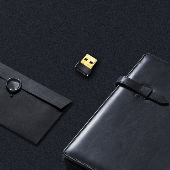 Gold and black USB wireless adapter placed on black surface between black envelope and leather organizer