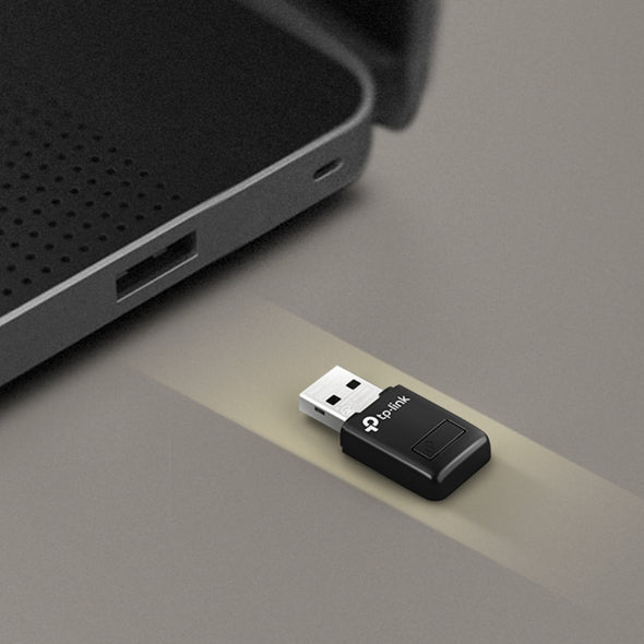 TP-Link USB WiFi adapter positioned near laptop USB port on a grey surface
