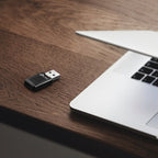 TP-Link USB Wi-Fi adapter on wooden desk next to silver laptop keyboard